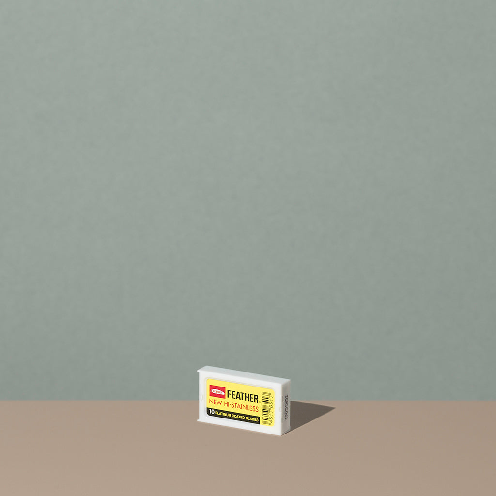 Feather safety razor blades in a small rectangle white plastic container with a yellow sticker labeling
