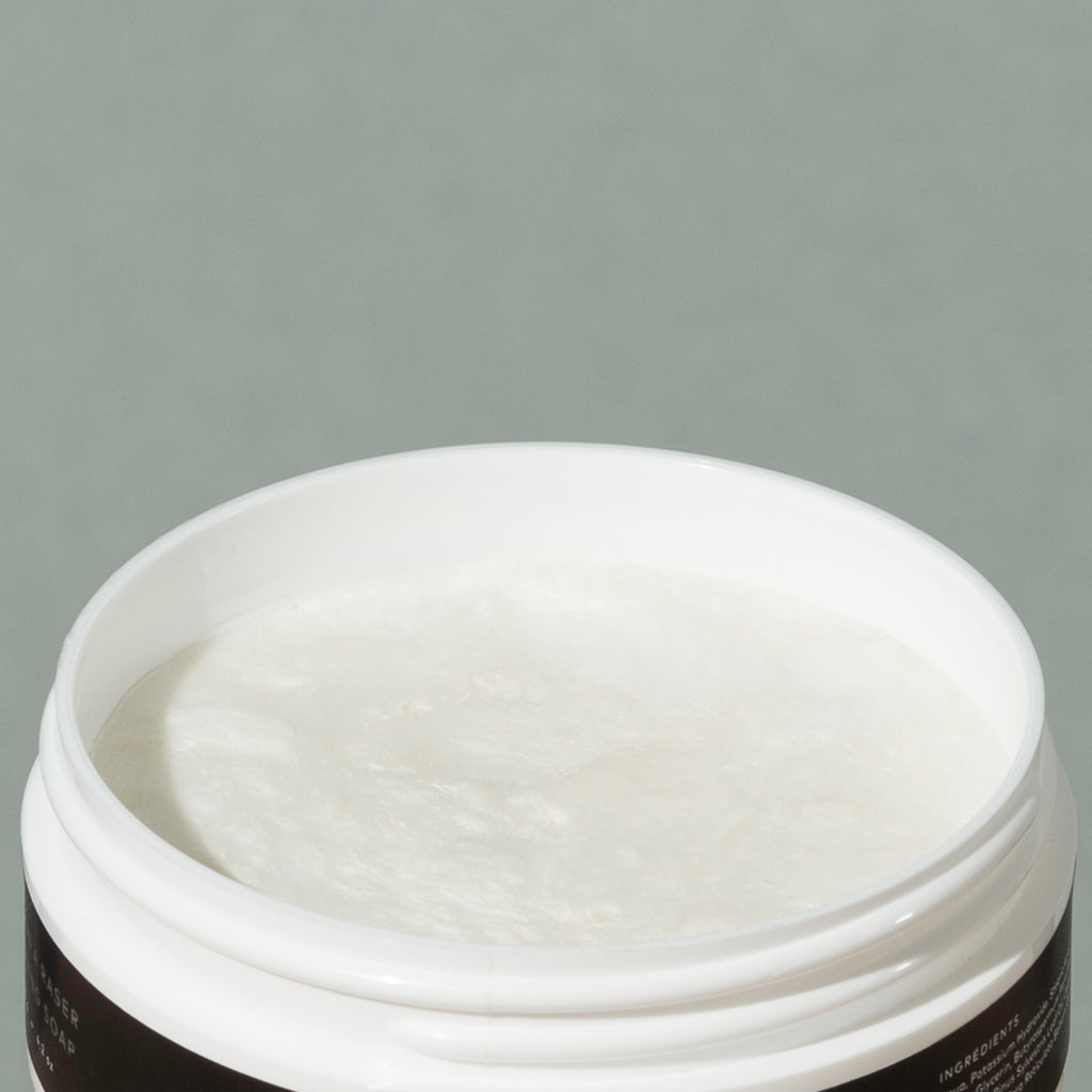 View inside creamy white Groom shaving cream in a round white plastic container packaging with a white and black label with a mustache man logo
