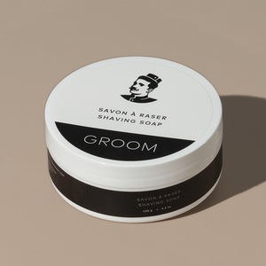 Groom shaving cream in a round white plastic container packaging with a white and black label with a mustache man logo