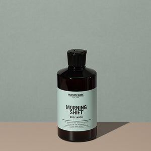 Hudson Made co Morning shift body wash in a amber rounded cylindric plastic bottle with a black flip top cap and green labeling