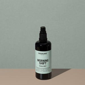 Hudson Made co Morning shift facial mist in a amber rounded cylindric plastic bottle with a black spray cap and green labeling