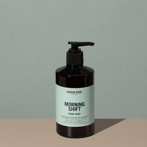 Hudson Made co Morning shift hand soap in a amber rounded cylindric plastic bottle with a black press down dispenser cap and green labeling