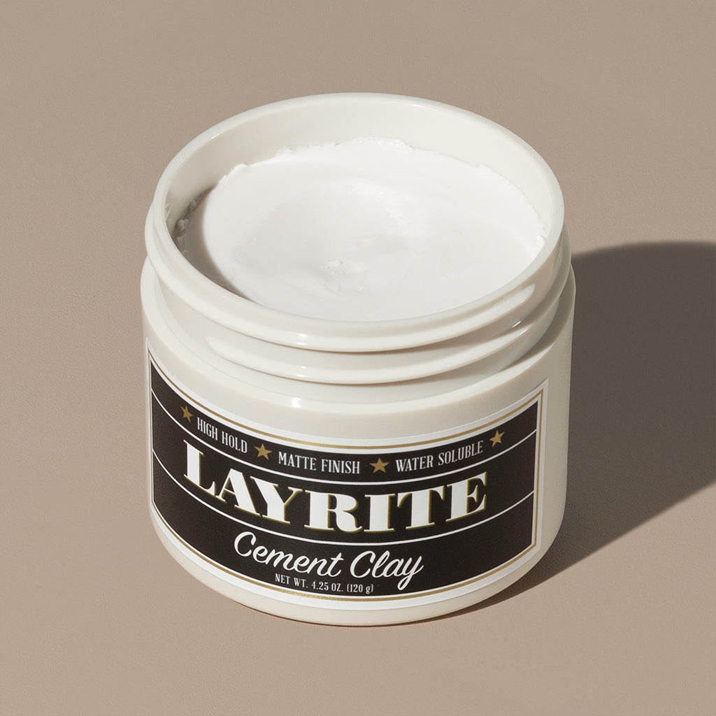 View inside white cream wax Layrite 4.25oz Cement Clay Extreme Hold and Matte Finish hair pomade in a rounded white plastic container with gold twist cap and black label