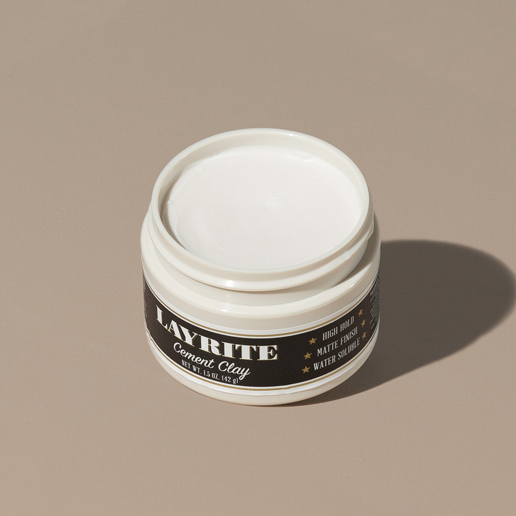 View inside white cream wax Layrite 1.5oz Cement Clay Extreme Hold and Matte Finish hair pomade in a rounded white plastic container with gold twist cap and black label