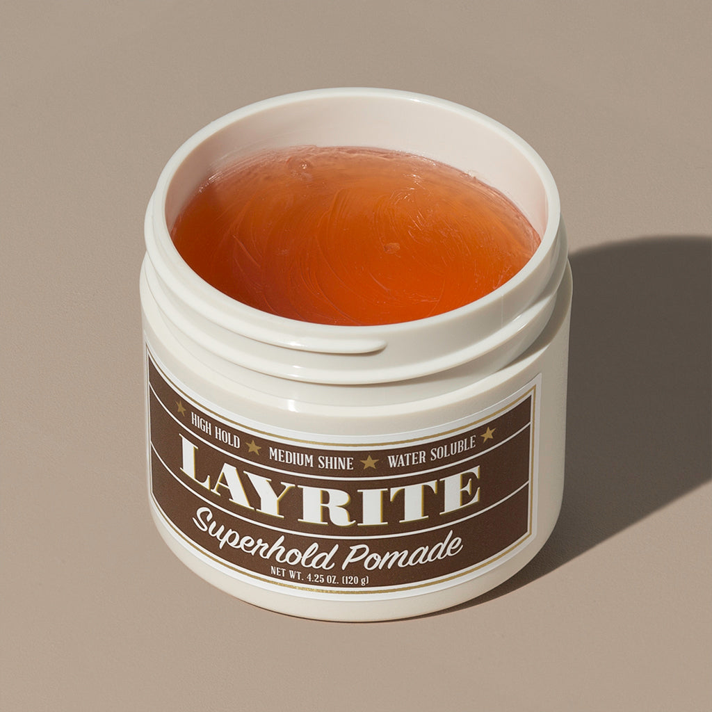 View inside transparent brown wax gel Layrite 4.25oz Superhold Pomade - High Hold & Medium Shine hair pomade in a rounded white plastic container with gold twist cap and brown label