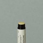 Close up details of yellowish wax Salt & Stone mint lipstick balm in a small cylindric black lipstick packaging with a black cap and off white labeling with black writings