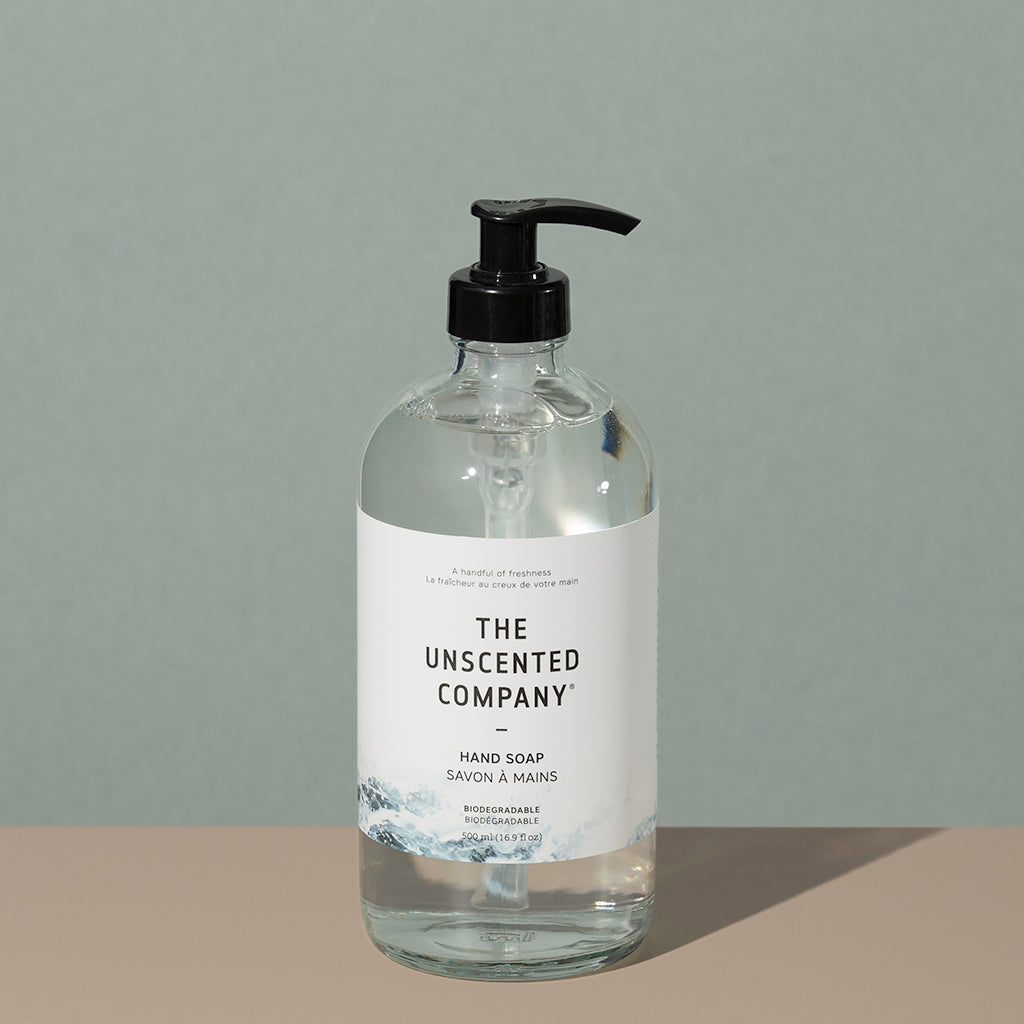 The Unscented Company biodegradable Hand soap in a clear glass bottle with a press down black dispenser cap and a white labeling with black writings and foggy gray mountains