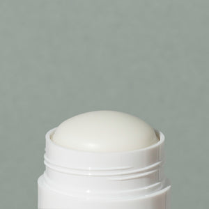 Close up details of white wax creamy Ursa Major base layer deodorant in a white small cylindric plastic container with a cap and green labeling of mountains