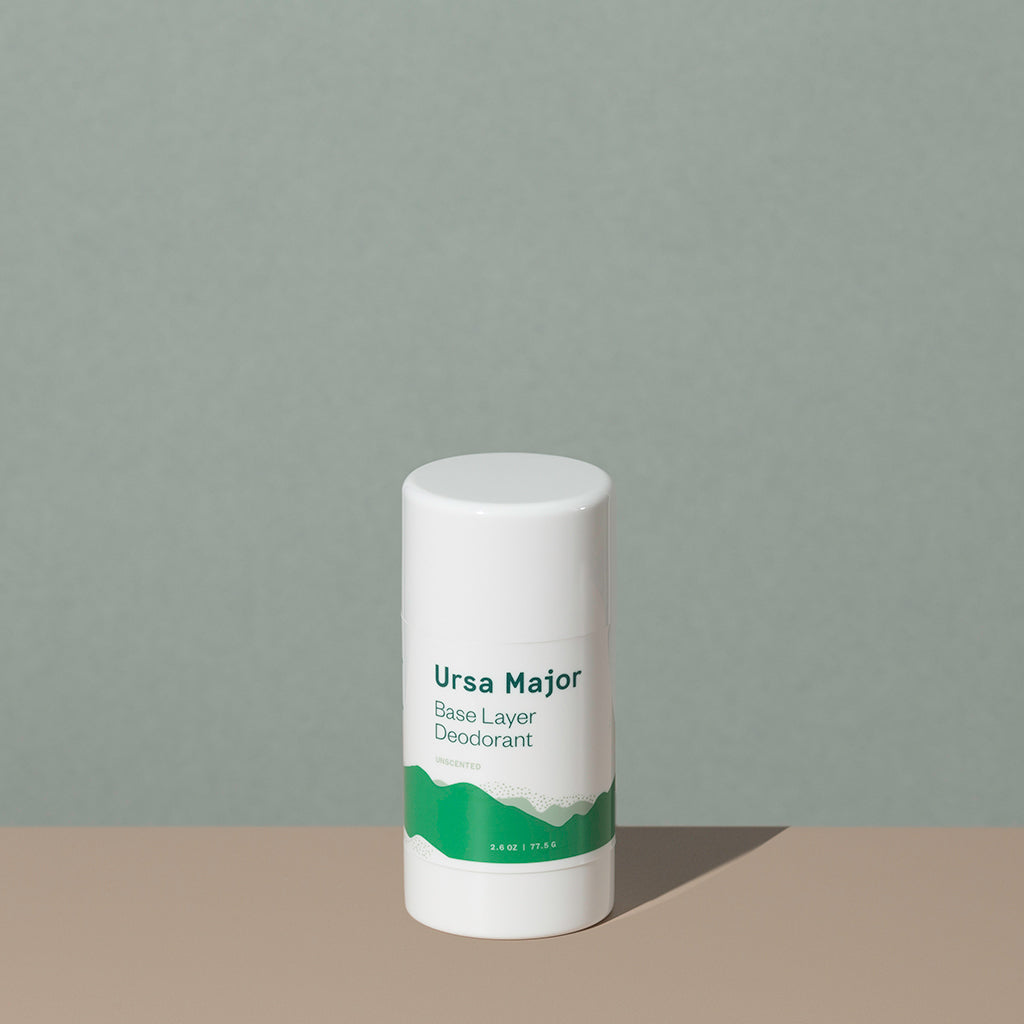 Ursa Major base layer deodorant in a white small cylindric plastic container with a cap and green labeling of mountains